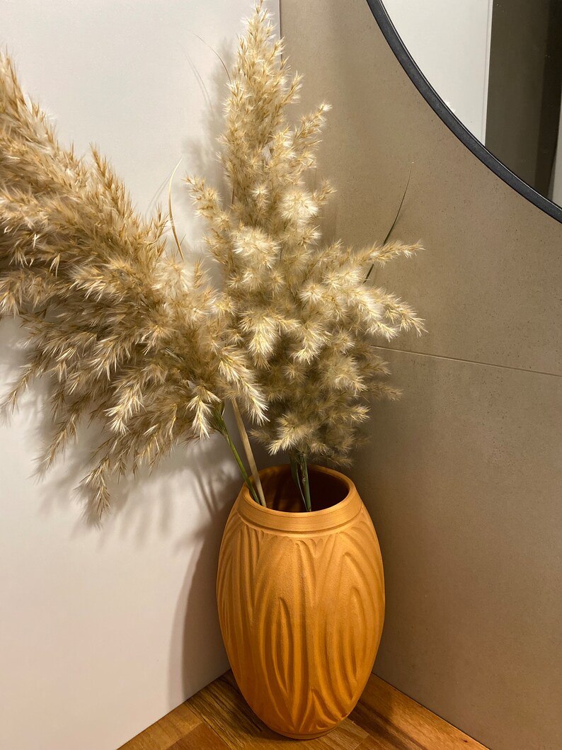 May include: A tall, brown ceramic vase with a textured, ribbed design. The vase is filled with dried pampas grass.