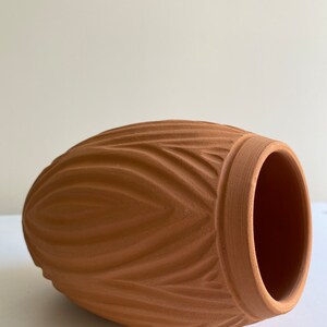May include: A terracotta vase with a ribbed design. The vase is a light brown color and has a rounded shape.