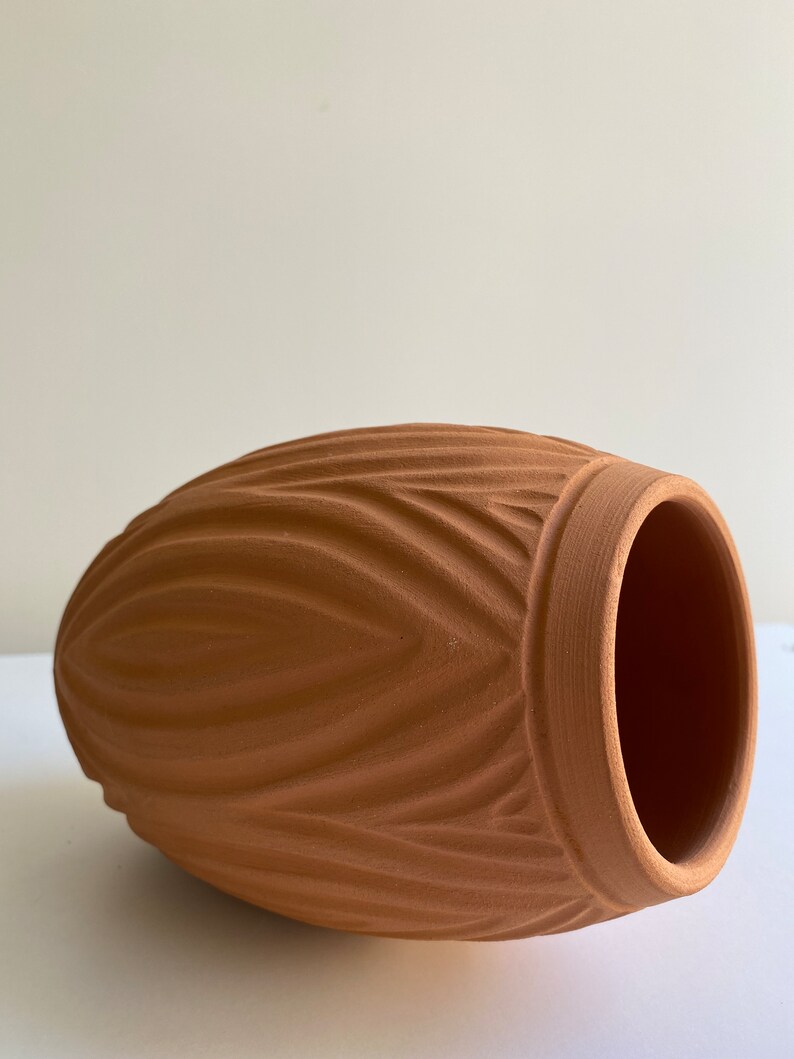 May include: A terracotta vase with a ribbed design. The vase is a light brown color and has a rounded shape.