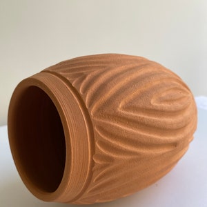 May include: A terracotta vase with a wavy, textured design. The vase is a light brown color and has a round shape.