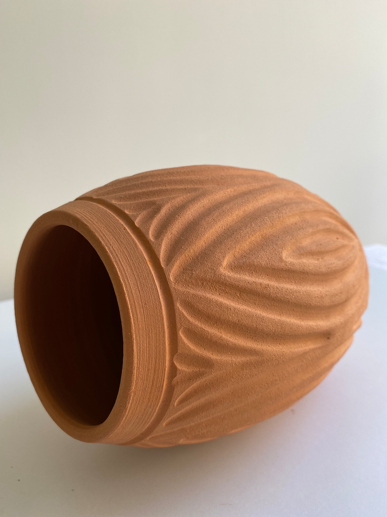 May include: A terracotta vase with a wavy, textured design. The vase is a light brown color and has a round shape.