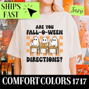 May include: Ivory-colored t-shirt with the text "ARE YOU FALL-O-WEEN DIRECTIONS?" and three cartoon ghosts at desks. The shirt also has the words "COMFORT COLORS 1717" at the bottom. The shirt is a Halloween-themed item.