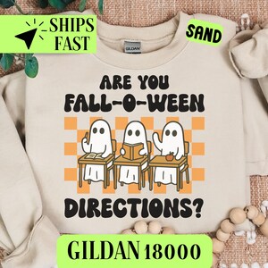 May include: Sand-colored sweatshirt with the text "ARE YOU FALL-O-WEEN DIRECTIONS?" and three cartoon ghosts at desks. The sweatshirt also has the text "GILDAN 18000".