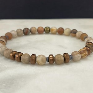 May include: A beaded bracelet featuring a mix of natural stone beads in shades of beige, brown, and copper. The bracelet includes copper-colored metal accents and measures approximately 7 inches in circumference.
