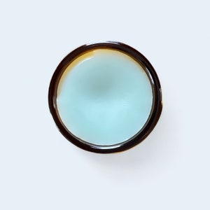 May include: A small round jar with a brown lid and a light blue balm inside.