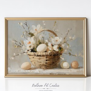 May include: A framed vintage print featuring a still life of a woven basket filled with white flowers and eggs. The artwork has a soft, muted color palette with a gold frame. The text "Northern Art Creative" is visible.