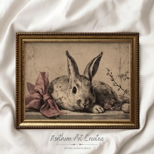 May include: A framed vintage print featuring a detailed illustration of a rabbit with long ears, a pink bow, and floral accents. The artwork is in a gold frame and has the text "Northern Art Creative" at the bottom.