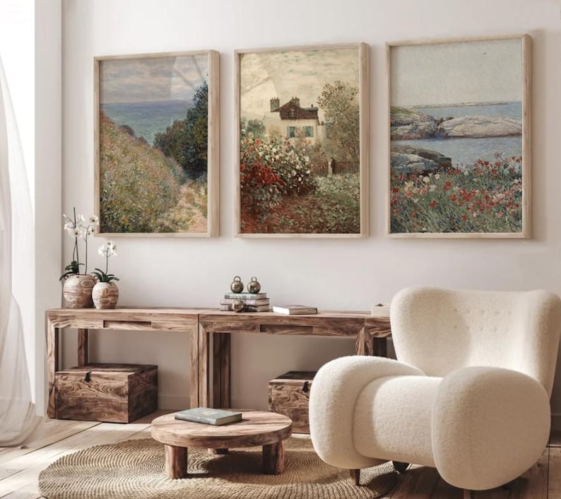 Puede incluir: Tres pinturas de paisajes enmarcadas con un tema costero. Las pinturas est&aacute;n en un sal&oacute;n con un sill&oacute;n blanco y una mesa de caf&eacute; de madera.