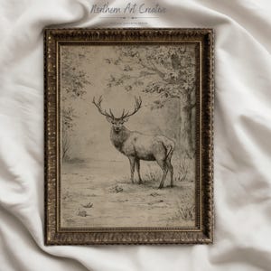 May include: A framed charcoal-style drawing of a stag standing in a forest clearing. The artwork features a detailed deer with large antlers, surrounded by trees and fallen leaves. The frame is ornate, metallic gold, and rectangular in shape.