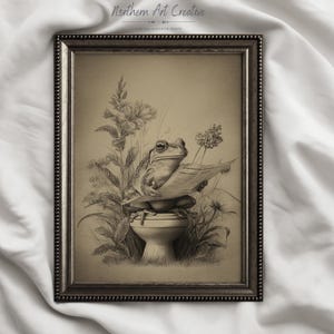 May include: Framed sepia-toned print featuring a frog wearing spectacles and reading a newspaper while seated on a toilet. The artwork includes floral and plant details, with the text "Northern Art Creative" at the top.
