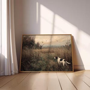 Peut inclure: Peinture de paysage encadr&eacute;e repr&eacute;sentant une sc&egrave;ne de chasse. Un chien avec des marques noires et blanches se tient dans un champ d'herbes hautes, avec un chasseur et des oiseaux en arri&egrave;re-plan. L'&oelig;uvre a une palette de couleurs chaudes et est expos&eacute;e sur un sol en bois.
