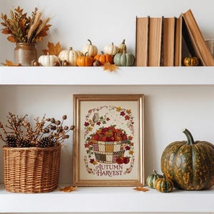 May include: A framed print featuring a basket of red apples, an owl, and autumn leaves with the text "AUTUMN HARVEST" in a gold frame. The print is displayed on a shelf with a wicker basket of dried branches and various pumpkins and gourds.