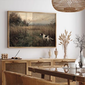 Peut inclure: Tableau vintage encadr&eacute; repr&eacute;sentant une sc&egrave;ne de chasse avec un chien dans un champ. L'&oelig;uvre d'art est encadr&eacute;e dans un cadre en bois marron et dor&eacute;. Le chien est blanc avec des taches marron. L'arri&egrave;re-plan montre un chasseur, des oiseaux et des herbes hautes.