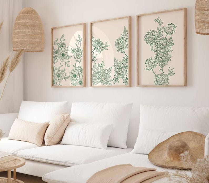 May include: Three framed prints with a white background and green floral illustrations. The prints are hanging on a white wall above a white sofa with cushions.