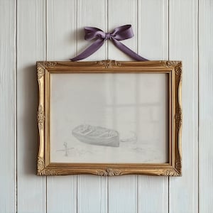 Op de afbeelding: Een ingelijste potloodtekening van een klein bootje op het water. De lijst is goudkleurig met sierlijke details en een paars lint is bovenaan om de lijst gebonden.
