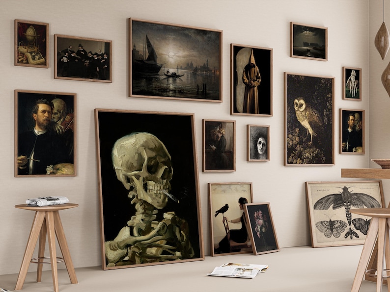 Puede incluir: Una pared de galer&iacute;a con una variedad de obras de arte enmarcadas, que incluyen una calavera, un b&uacute;ho, una figura encapuchada y un bodeg&oacute;n. Las obras de arte se exhiben en una pared blanca con un suelo de madera.