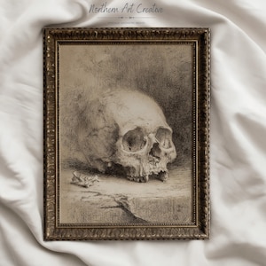 May include: A framed sepia-toned art print featuring a detailed sketch of a human skull resting on a ledge. The ornate, dark gold-colored frame surrounds the drawing, which includes the text Northern Art Creative and VINTAGE AESTHETIC PRINTS.