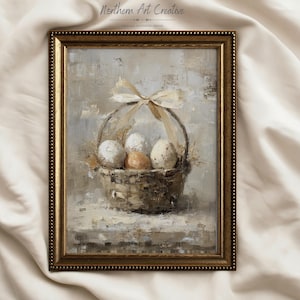 Può includere: Stampa estetica vintage incorniciata con un cesto di uova. Il cesto, legato con un fiocco color crema, contiene uova bianche e marroni macchiate. L'opera d'arte ha una tavolozza di colori neutri e una cornice dorata. Il testo "Northern Art Creative" è visibile.