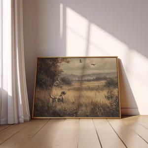 May include: A framed landscape painting featuring a hunting scene with a dog in a field of tall grass. The artwork has a muted color palette with a dog, hunter, and birds in the sky. The frame is a light brown color.