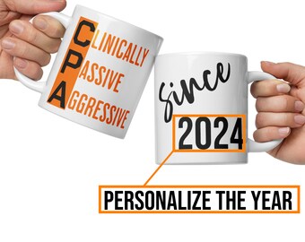Op de afbeelding: Een witte keramische mok met de tekst "Clinically Passive Aggressive" in oranje letters en de tekst "since 2024" in zwarte letters. Het jaar kan worden gepersonaliseerd.