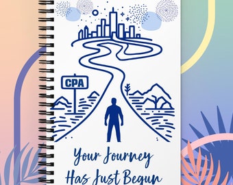 Op de afbeelding: Een wit notitieboek met spiraalbinding en een blauwe illustratie van een persoon die op een pad staat dat naar een skyline leidt met de tekst "CPA" op een wegwijzer. De tekst "Your Journey Has Just Begun" staat onder de illustratie.