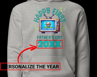 Op de afbeelding: Grijze hoodie met een retro-tv-afbeelding met de tekst "Happy First Father's Day 20XX". De tv toont een gepixelde figuur en de tekst "Level 1 Unlocked".
