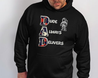 Op de afbeelding: Zwarte hoodie met de witte tekst "DUDE DAD ALWAYS DELIVERS". De letters D, A en D hebben een rood, wit en blauw ontwerp. Een illustratie van een astronaut staat naast de tekst. De hoodie heeft een voorzak.