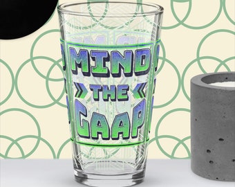 Op de afbeelding: Een helder glazen pintglas met een groene en blauwe afbeelding met de tekst "Mind the Gap".