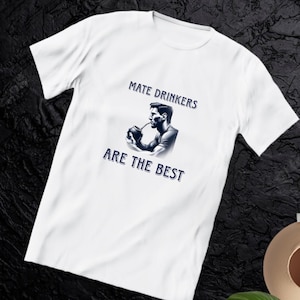 Peut inclure: T-shirt blanc avec le texte "MATE DRINKERS ARE THE BEST" en bleu. Le t-shirt présente un graphisme d'une personne buvant du maté. Le t-shirt est fait d'une matière douce.
