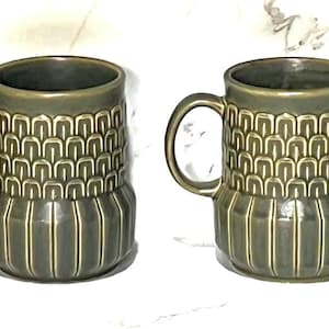 May include: Six olive green ceramic mugs with handles. The mugs have a textured pattern on the upper half and vertical lines on the lower half. The mugs are arranged in a row against a white background.