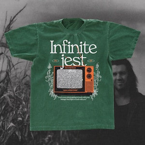 Può includere: T-shirt verde con la scritta "Infinite Jest" in bianco. Sotto, una grafica di un televisore vintage arancione con statico. La maglietta include anche il testo "RECDYE WITHOUT DYING" e "Don't worry about getting in touch with your feelings, they'll get in touch with you."
