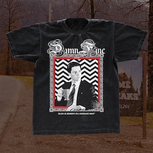May include: Dark grey t-shirt featuring a black and white graphic of a man in a suit holding a cup, within a red and white zig-zag border. The shirt has the text "Damn Fine" and "Black as Midnight on a Moonless Night".