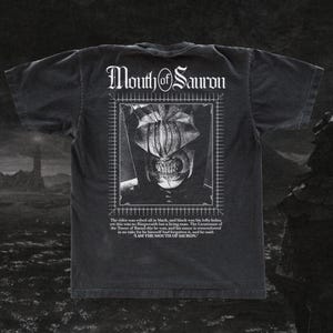 May include: A black short-sleeve t-shirt featuring a white graphic print of the Mouth of Sauron. The design includes a framed portrait, the text "Mouth of Sauron" at the top, and a quote from the character printed in white text below the image.