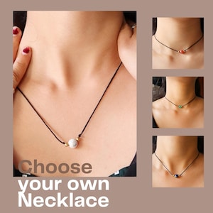 May include: Choose your own necklace. Three necklaces with different coloured stones on a black cord. The first necklace has a white stone, the second has a red stone, and the third has a green stone.