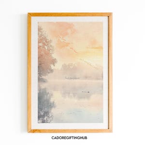 Op de afbeelding: Een ingelijste print met een aquarelachtige afbeelding van een meer met een boom aan de linkerkant van de afbeelding. Het meer is omgeven door mist en de lucht heeft een zachte oranje kleur. De tekst "Slow Down, Go Slow, Don't Worry, Don't Hurry, Trust the Process" staat in de afbeelding.