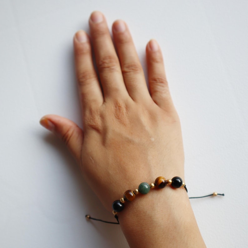 May include: A black string bracelet with gold beads and tiger's eye, green, and black gemstone beads.