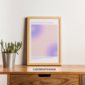 May include: A framed print with a pink and purple gradient background. The text "TRANSCENDANT ENERGY" is at the top of the print. The text "Use the universes energy to transcend all upper limits. Your goals are yours." is at the bottom of the print. The text "CADOREGIFTINGHUB" is below the frame.