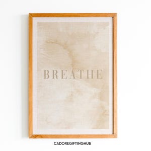 May include: A framed print with a beige background and the word "BREATHE" in a light gray font. The frame is made of wood and has a natural finish.