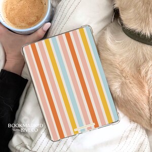 May include: A clear case for a tablet with a colorful striped design in pink, orange, yellow, and blue. The case has the text "BOOKMARKED WITH LOVECO" on the bottom left corner.