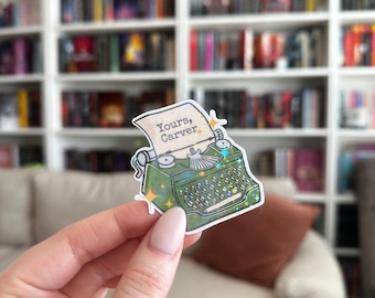 Peut inclure: Un autocollant de machine à écrire vert avec une note qui dit "Yours, Carver." L'autocollant a des accents de paillettes et est tenu dans une main.