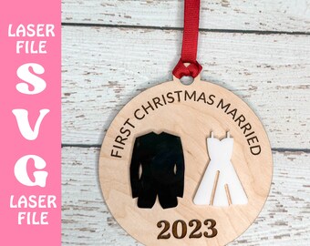 Puede incluir: Adorno navideño de madera con el texto "First Christmas Married" y el año "2023". El adorno presenta un esmoquin negro y un vestido de novia blanco. Se adjunta una cinta roja para colgarlo. Las palabras "Laser File" y "SVG" están a la izquierda.
