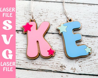May include: Two wooden ornaments shaped like the letters K and E. The K is pink with a pink star and the E is blue with a light blue star. Both ornaments have a string for hanging.