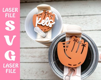 Może przedstawiać: Dwa brązowe charms do pokrywek do napojów w kształcie rękawicy baseballowej, jeden z nich z napisem "Kels". Charms znajdują się na dwóch kubkach ze stali nierdzewnej z pokrywkami i słomkami.