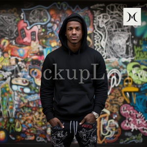 May include: A black hooded sweatshirt with a pouch pocket. The sweatshirt is being worn by a person standing in front of a colourful graffiti wall.