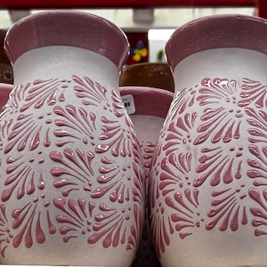 May include: Two ceramic vases with a white base and a pink floral design. The rims are pink. The vases have a textured, raised pattern. The vases are likely for decorative purposes.