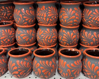 Könnte beinhalten: Eine Sammlung handgefertigter Keramikbecher. Die Becher sind grau mit orangefarbenen floralen Designs und orangefarbenen Rändern. Die Becher sind aufeinander gestapelt und zeigen die komplizierten Details der Keramik.