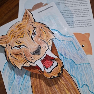 Puede incluir: Ilustración colorida de un tigre dientes de sable con la boca abierta. La imagen es de un libro infantil titulado "Sunset of the Sabertooth". El fondo incluye texto sobre las edades de hielo y una ilustración azul y marrón.