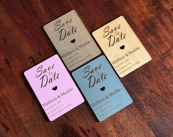 Puede incluir: Cuatro tarjetas de madera para guardar la fecha con un corazón recortado. Las tarjetas son de color rosa, azul, marrón y marrón claro. El texto de las tarjetas dice "Save the Date" con los nombres "Matthew & Maddie" y la fecha "November 4, 2025".