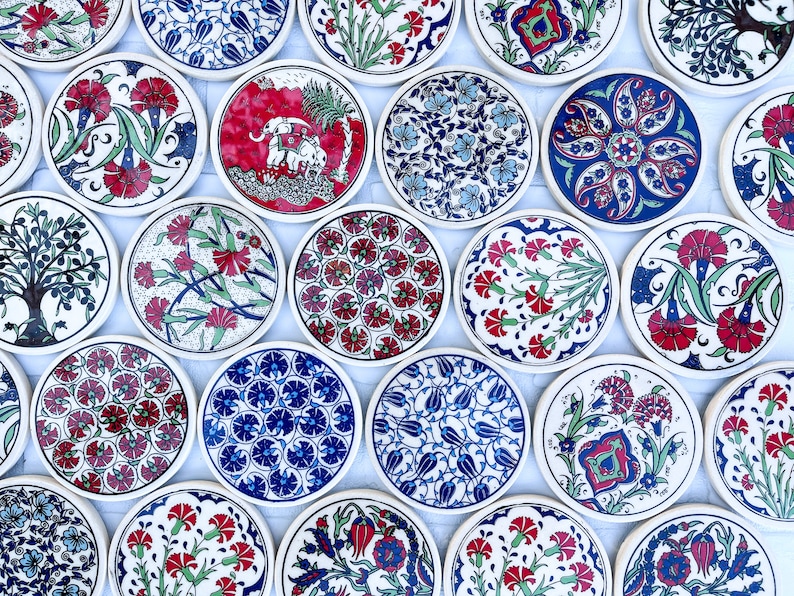May include: A collection of round ceramic coasters with intricate floral and geometric designs in shades of blue, red, and green. The coasters are arranged in a circular pattern on a white surface.