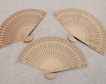 May include: Three wooden hand fans with intricate cut-out designs. The fans are closed and arranged in a triangular pattern on a light beige surface.